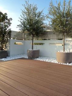 a wooden deck with two planters and trees in the back ground, next to a white fence