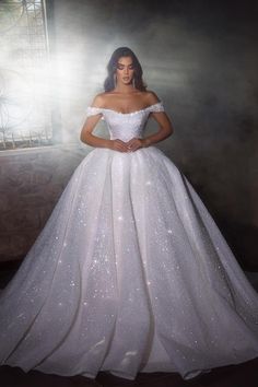 a woman in a white wedding dress standing next to a window with her hands on her hips