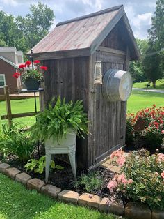 an outhouse with potted plants and flowers in the front yard, next to a flower bed