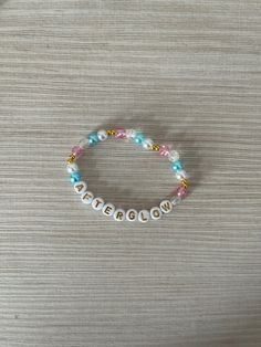 a white beaded bracelet with blue and pink beads on top of a wooden table