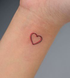 a small heart tattoo on the wrist is shown in black and red ink, with a thin line at the center