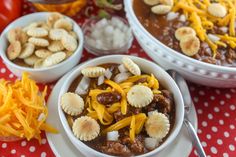 three bowls filled with chili cheese and crackers on top of a table next to other dishes