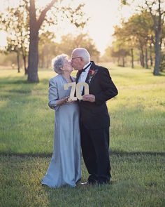 an older couple kissing each other while standing in the grass with trees and sunlight behind them