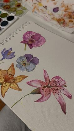 a person holding a paintbrush in their hand and painting flowers on the paper with watercolors