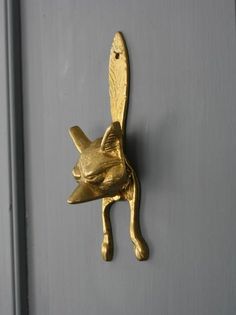 a gold cat head mounted on the side of a gray wall with a hook in it's mouth