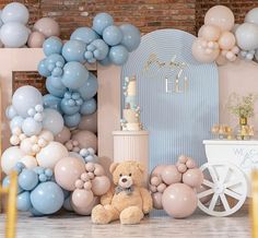 there is a teddy bear sitting in front of balloons on the wall, and an arch