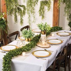 the table is set with white and gold plates, greenery, and candle holders