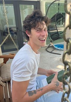 a young man is sitting on a swing and smiling at the camera while holding a hair dryer in his hand