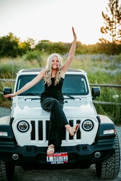 a woman sitting on the hood of a white jeep with her arms in the air