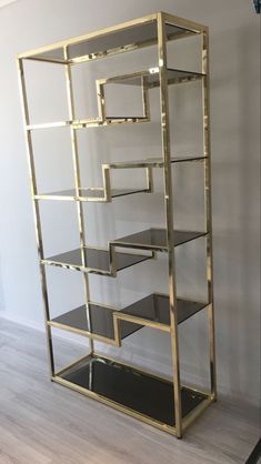 a gold and black shelving unit with glass shelves on the bottom, in front of a white wall