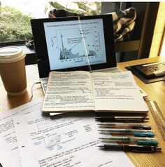 an open book sitting on top of a wooden table next to a laptop and pen