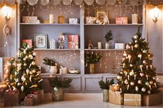 two christmas trees sitting in front of bookshelves with presents on the shelves behind them