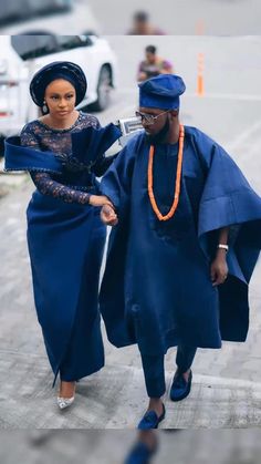 two women dressed in blue are walking down the street with one woman wearing an orange necklace