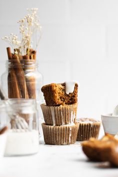 muffins with icing and cinnamon sticks in glass jars on a white table