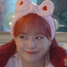 a girl with red hair wearing a pink bunny ears headband and smiling at the camera