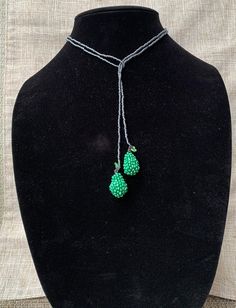 a black mannequin with two green beads hanging from it's neckline