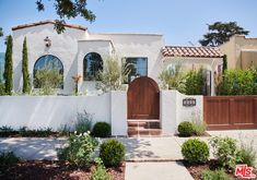 a white house with brown doors and trees in the front yard on a sunny day