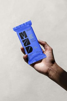 a hand holding up a blue bag of naxo energy bar in front of a white wall