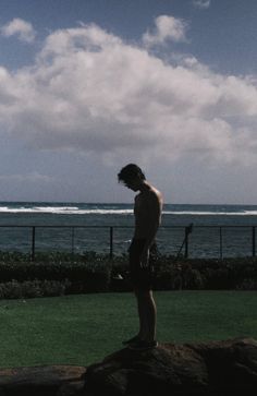 a man standing on top of a lush green field next to the ocean