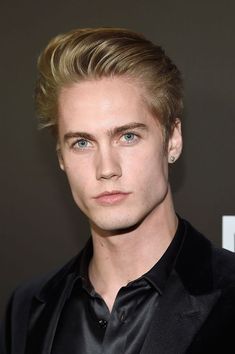 a young man with blonde hair wearing a black suit and bow tie at an event