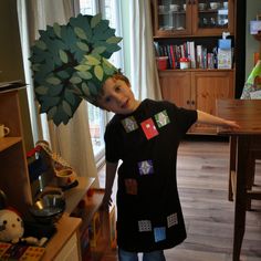 a young boy standing in front of a table with a paper tree on it's head