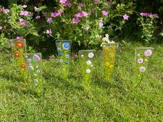 four glass vases sitting in the grass near flowers