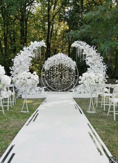 an outdoor wedding setup with white flowers and greenery on the aisle, surrounded by tall trees