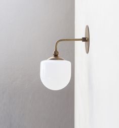 a white wall mounted light on the side of a door with a metal arm and round glass shade