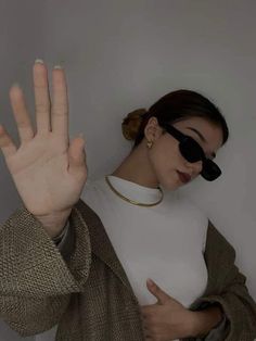 a woman with her hand up in front of her face, wearing sunglasses and a white shirt