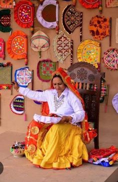 a woman sitting on top of a wooden chair in front of a wall covered with colorful items