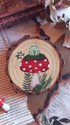 a wooden slice with a frog sitting on top of it next to mushrooms and leaves