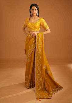 Editor's Note A mustard yellow zardozi embroidered dupion silk sari and blouse would be a stunning choice for a traditional event or wedding. The rich and vibrant color paired with intricate zardozi embroidery would make for a gorgeous and elegant ensemble. Color: Mustard yellow Fabric: Dupion silk & chanderi Embroidery details: Zardozi embroidery Components: Sari & blouse Sari length: 6 meters, sari width: 46" inches Occasion: Festive and Wedding Guest Disclaimer: Product color may slightly var Gold Pre-draped Saree With Cutdana For Navratri, Fitted Yellow Pre-draped Saree With Pallu, Yellow Unstitched Sharara For Transitional Season, Traditional Chinon Blouse With Dupatta, Designer Pre-draped Yellow Saree, Festive Yellow Raw Silk Pre-draped Saree, Yellow Pre-draped Saree For Festivals, Gold Pre-draped Saree For Reception, Transitional Gold Sharara With Dori Work