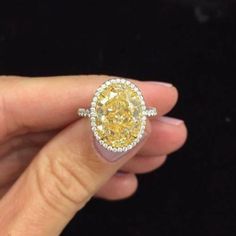 a woman's hand holding an oval yellow diamond ring with diamonds around the band