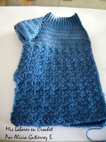 a crocheted blue sweater sitting on top of a white table next to a ball of yarn