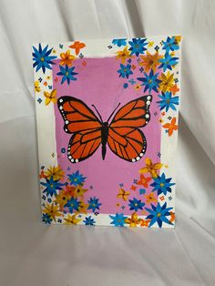 an orange butterfly painted on a pink background with blue, yellow and red flowers around it