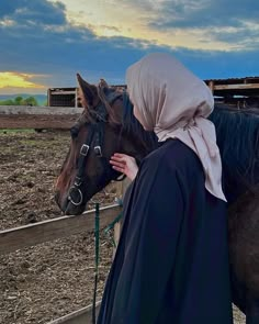 a woman in a hijab is standing next to a horse and looking at the sky