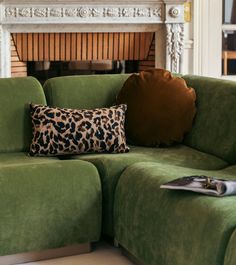 a green couch sitting in front of a fire place with a leopard print pillow on it