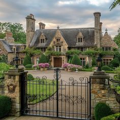 a gated in driveway leading to a large house with lots of bushes and flowers