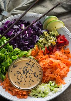 a white plate topped with different types of veggies and dipping sauce next to chopsticks