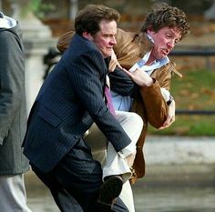 two men in suits and one is holding another man on his back as they walk down the street