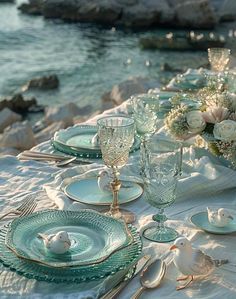 the table is set with white flowers and blue glassware for an elegant dinner by the water