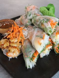 a plate with shrimp, carrots and rice rolls next to dipping sauce on the side