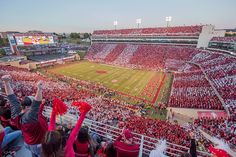 a football stadium filled with people and fans holding up red pom poms in the air