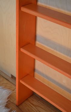 an orange book shelf sitting on top of a hard wood floor next to a wall