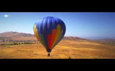 a hot air balloon flying in the sky over a desert area with mountains and trees