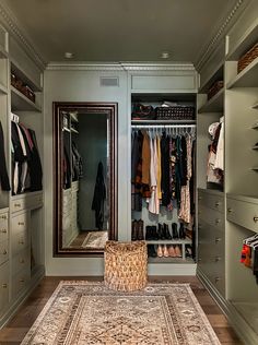 a walk in closet with an area rug and clothes hanging on the wall, along with two large mirrors