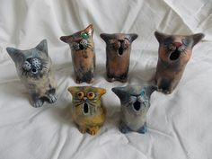 five ceramic cats sitting on top of a white cloth covered tablecloth, each with different colored eyes