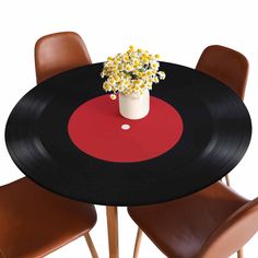 a vase with flowers sitting on top of a black table next to two brown chairs