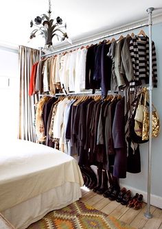 a closet with clothes hanging on the wall and a bed next to it in front of a chandelier