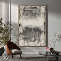 an abstract painting hangs on the wall next to a chair and table in a modern living room